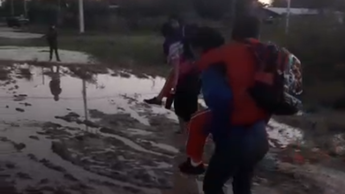 Madres cargan a sus hijos para cruzar camino inundado y llegar a la escuela en Puerto Casado